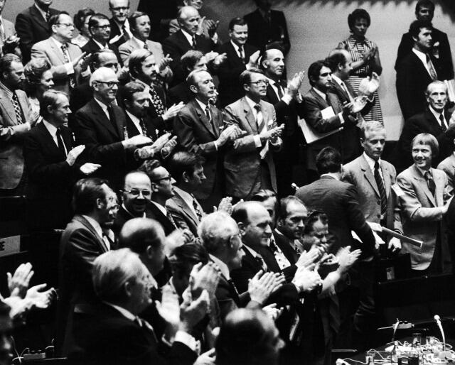 Black and white photo of a standing ovation in a formal setting with men and women applauding.